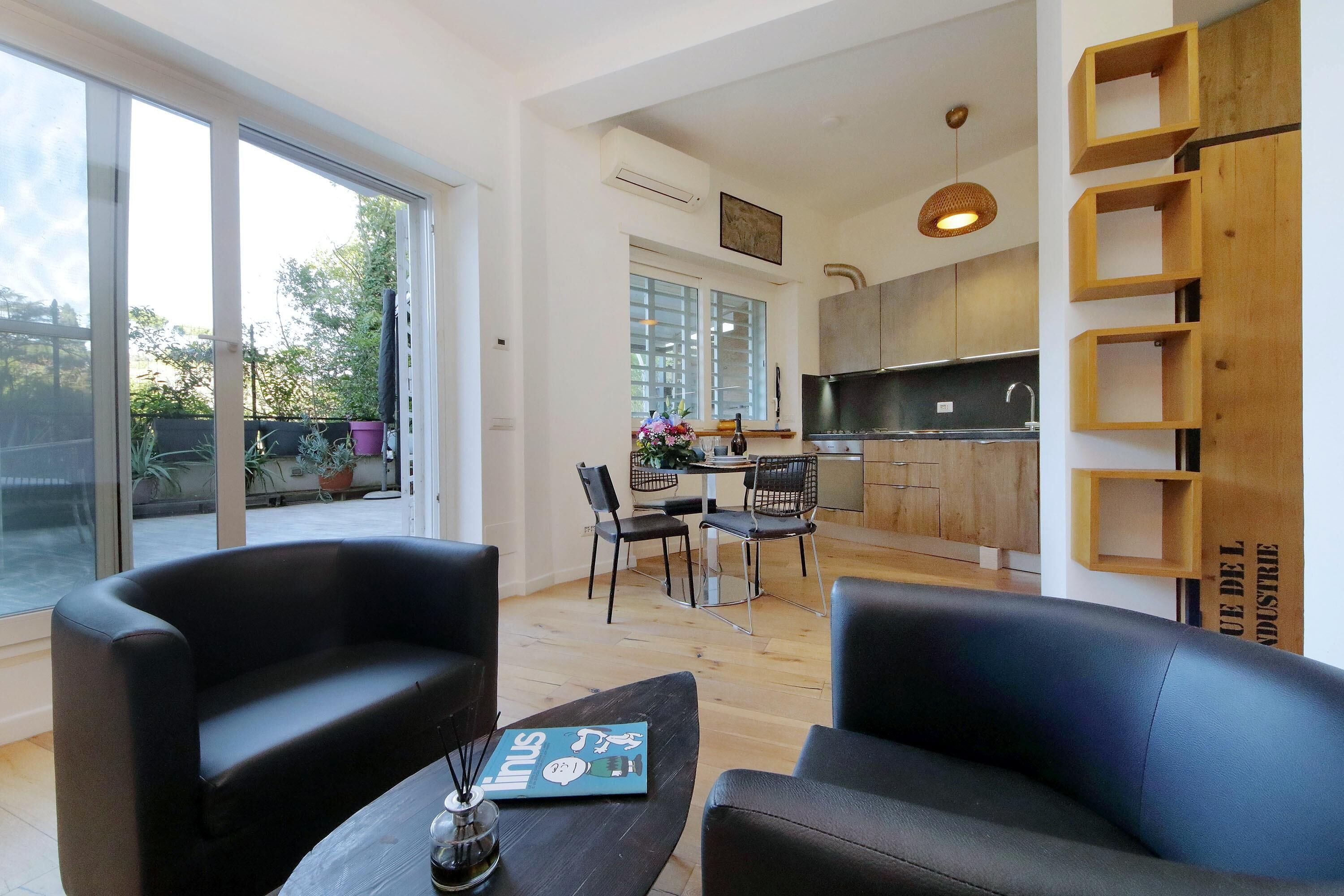 A modern living room with a large window, a dining area, and a kitchen.