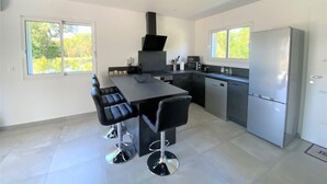 Cozinha moderna com ilha central, banquetas pretas, forno embutido e geladeira de aço inoxidável.