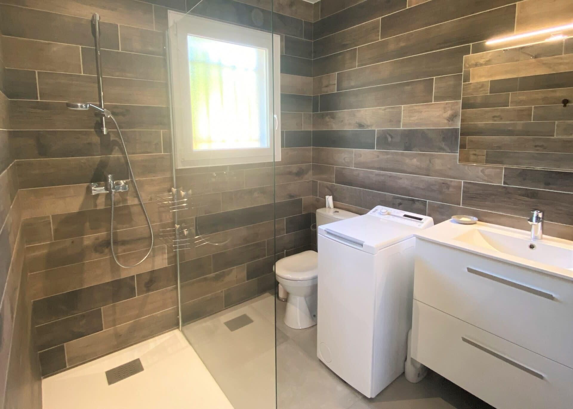 A modern bathroom with a glass-enclosed shower, a toilet, and a washing machine.