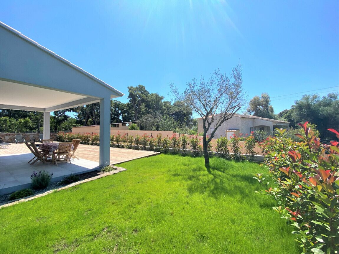 Un patio couvert aménagé avec du mobilier d’extérieur, une pelouse bien entretenue et une variété de plantes.