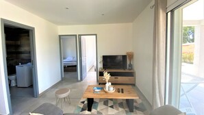 Uma sala de estar moderna com um sofá, uma mesa de centro e uma televisão. Há uma porta de correr que dá para um banheiro e uma varanda com vista.