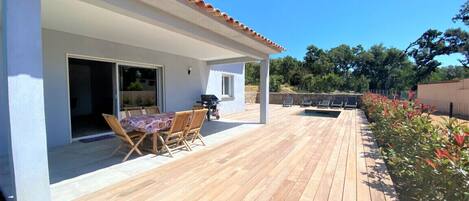 A wooden deck with a table and chairs, a covered patio area, and a stone wall in the background.