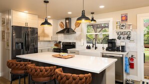 Una cocina moderna con una isla grande, electrodomésticos de acero inoxidable, iluminación colgante y vistas al exterior.