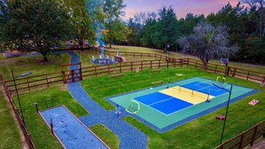 Un espacio deportivo al aire libre cercado, con cancha de baloncesto, piscina pequeña y sendero para caminar.