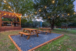 Een terras met houten picknicktafels en een pergola met lichtslingers.