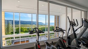 A gym with stationary bikes and a treadmill, large windows with a view of a landscape.