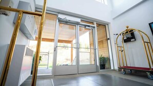 A hotel entrance with a sliding glass door, a golden luggage cart, and a view of the outdoor area.