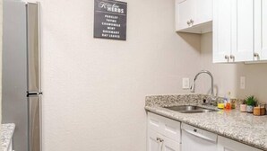 A kitchen with white cabinets, a granite countertop, a stainless steel refrigerator, and a sign listing herbs. - Cozy 1Bed 1Bath Apt by Downtown & Farmers Market (Houston)
