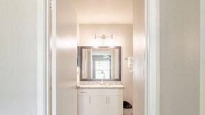 A hallway leading to a bathroom with a white vanity, a mirror, and a light fixture. - Tangerine 2Bed 2Bath at 5 min walk to NRG near TMC (Houston)