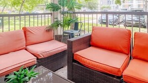 A covered outdoor seating area with wicker furniture and orange cushions, a glass table, and a potted plant. - Tangerine 2Bed 2Bath at 5 min walk to NRG near TMC (Houston)