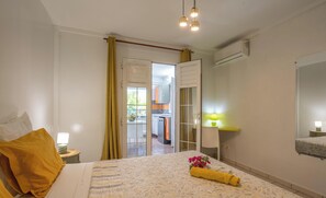 Une chambre à coucher comprenant un lit, une lampe de chevet, une fenêtre avec des rideaux, une porte donnant sur un balcon et un appareil de climatisation.