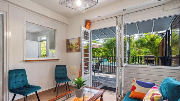 A living room with a sofa, two chairs, a coffee table, a potted plant, a painting, and a sliding glass door leading to an outdoor patio. - Just like home, private swimming pool not overlooked (Rivière-Salée)