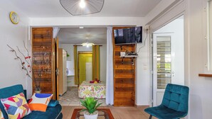 A living room with a sofa, a chair, a coffee table with a plant, a TV mounted on the wall, and a wooden door leading to another room. - Just like home, private swimming pool not overlooked (Rivière-Salée)
