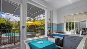 Una cucina con vista sulla piscina e sugli ombrelloni, un tavolo con un libro e una finestra che si affaccia sul verde.