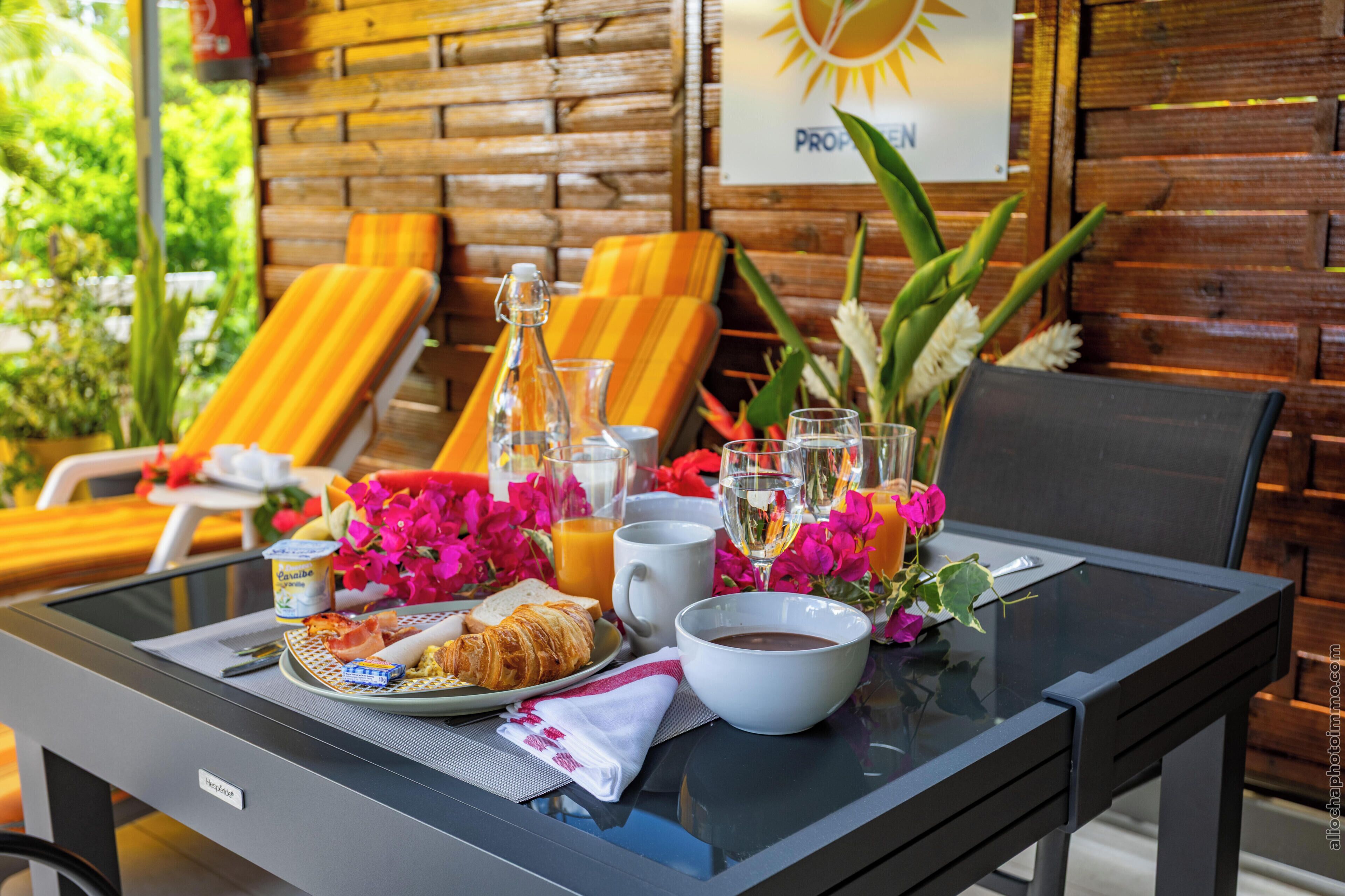 A breakfast table with croissants, a bottle, glasses, and a bowl of soup.
