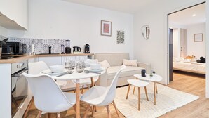 Una cocina moderna con armarios blancos, un comedor con sillas blancas, un sofá y una mesita auxiliar.