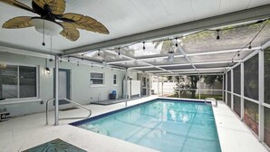 Una piscina techada con ventilador de techo, cerramiento de vidrio y vistas al exterior.