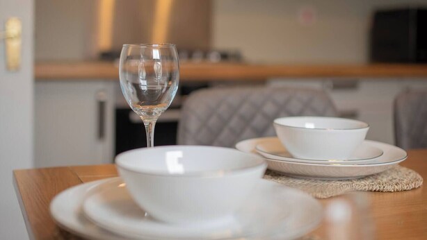 Une table à manger avec des assiettes blanches, des bols et un verre à vin, disposés sur une table en bois recouverte d’un set de table.