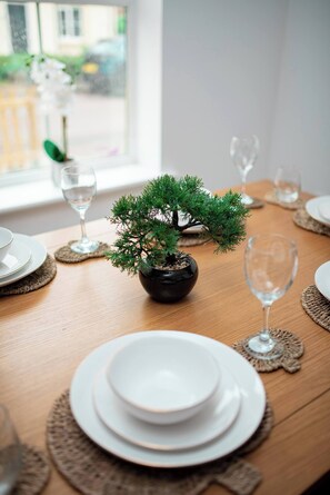 A neatly set dining table with white plates, a bonsai tree centerpiece, and clear glassware. - Light House (Sleeps 9) (Swindon)