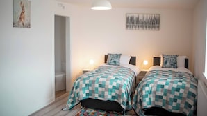 Une chambre à coucher avec deux lits, chacun recouvert d’une couvre-lit à carreaux, une table de chevet avec une lampe et un tableau accroché au mur.