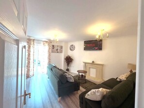 A living room with two sofas, a fireplace, a clock, and a wall-mounted TV displaying Netflix. - Light House (Sleeps 9) (Swindon)