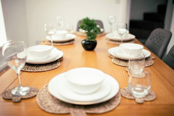 A dining table set with white plates, bowls, and glasses, with a small potted plant in the center. - Light House (Sleeps 9) (Swindon)