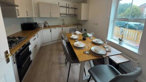 Une cuisine moderne avec des meubles blancs, un plan de travail en bois et un coin repas avec une table dressée pour quatre personnes.