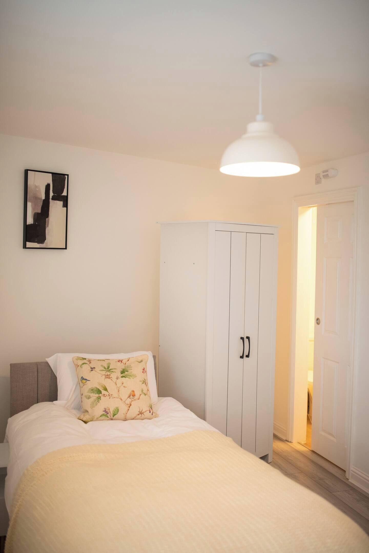 Un dormitorio con una cama, un armario blanco, una lámpara colgante y una puerta que da a otra habitación.