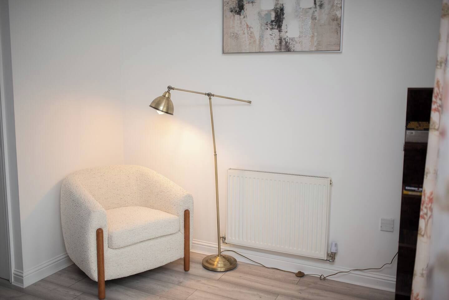 A room with a white armchair, a floor lamp, a radiator, and a painting on the wall.