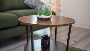 Un salon chaleureux avec un canapé vert, une table basse ronde en bois surmontée d’un terrarium en verre et une petite plante en pot.