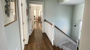 Un pasillo con suelo de madera, barandillas blancas y paredes azul claro.
