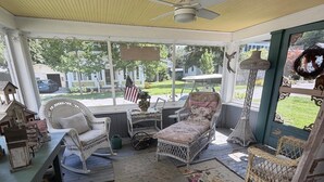 Eine überdachte Veranda mit Korbmöbeln, Deckenventilator und Blick auf den Garten.