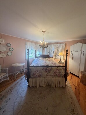 A bedroom with a four-poster bed, a chandelier, a dresser, and a window with curtains. - Cottage Close to the Lake! (Lakeside)