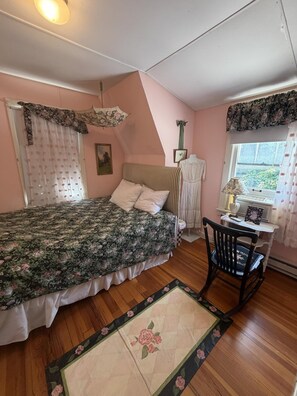 A bedroom with a bed, a chair, a window with curtains, a radiator, and a picture frame on the wall. - Cottage Close to the Lake! (Lakeside)