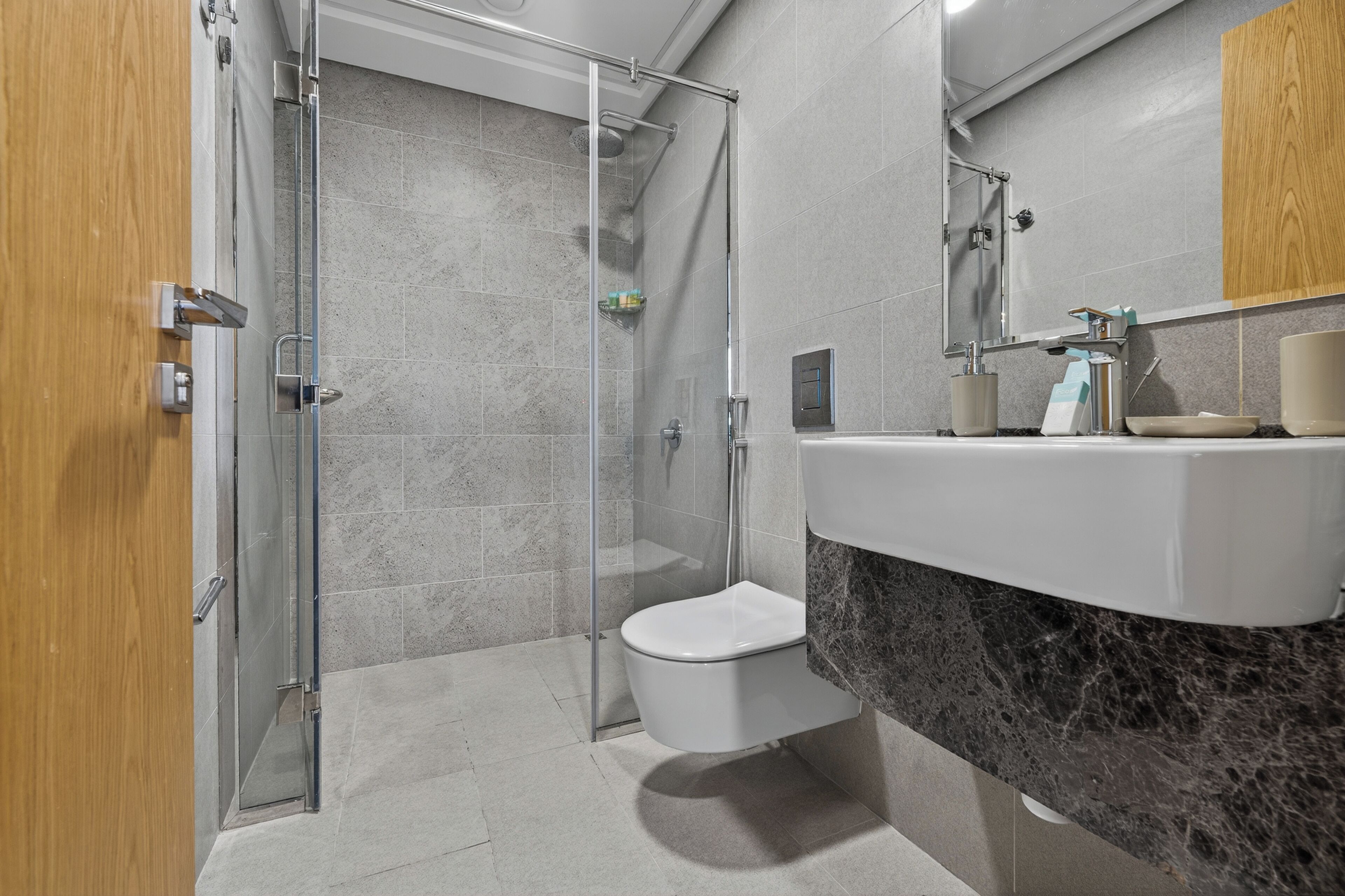 Ein modernes Badezimmer mit einer in Glas eingefassten Dusche, einer weißen Toilette und einer Marmorplatte mit Waschbecken und Spiegel.