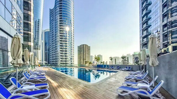 A rooftop pool area with lounge chairs and umbrellas, surrounded by high-rise buildings. - Radiant Boulevard by DVH Luxe Retreats (Abu Dhabi)