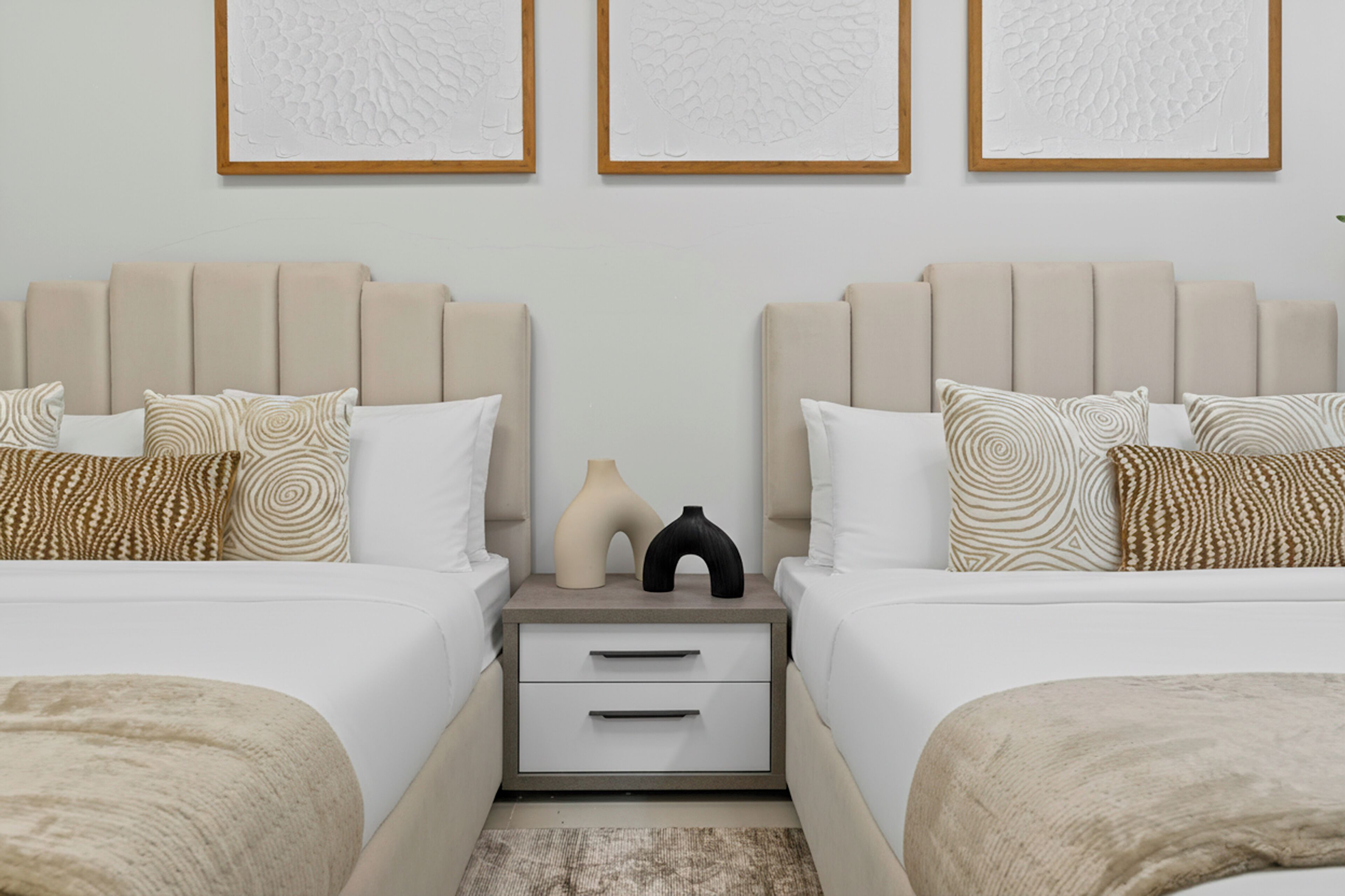 Ein Hotelzimmer mit zwei Betten, einem Nachttisch mit Schubladen und drei gerahmten Kunstwerken an der Wand.