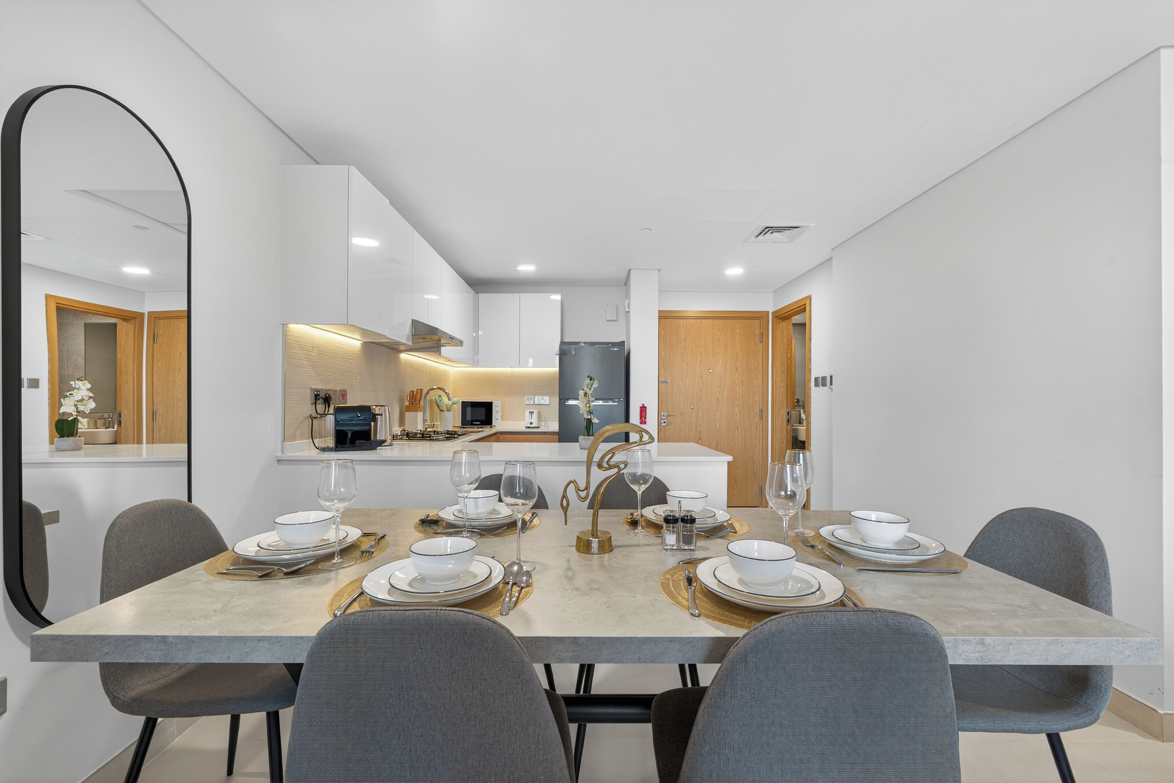 Un comedor moderno con una mesa de mármol, sillas grises y una cocina al fondo.