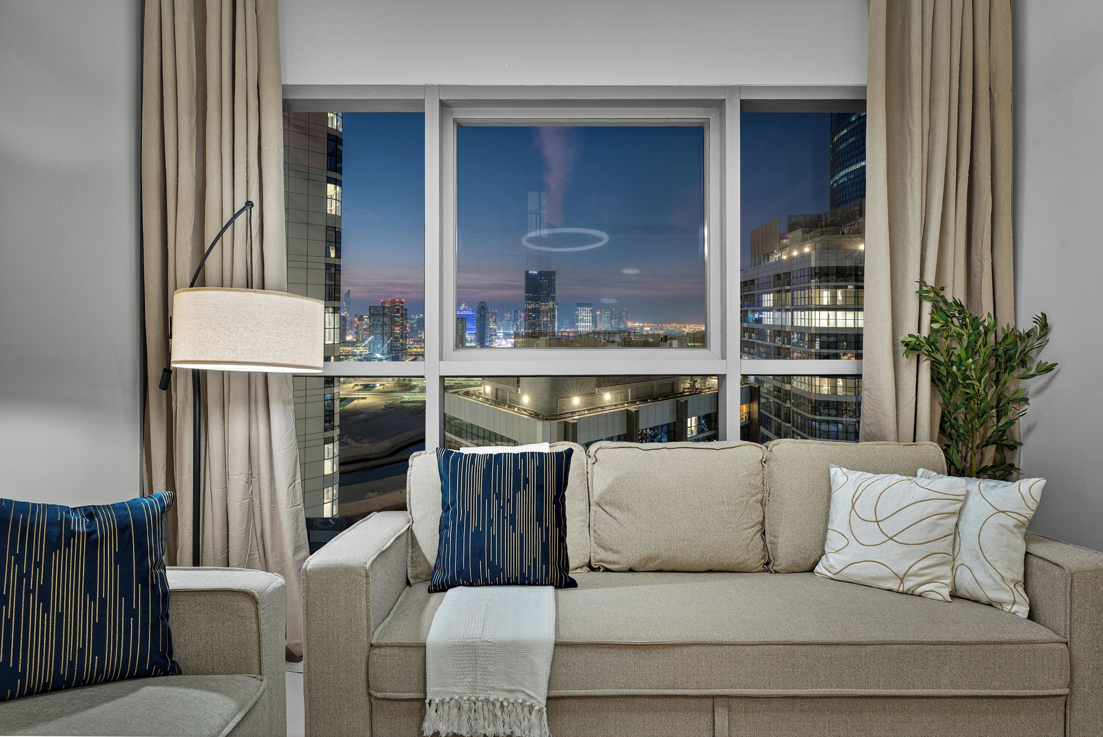 Un salon moderne avec vue sur la ville, comprenant un canapé, une lampe et une plante.