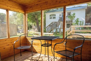 Um deck de madeira com uma mesa e duas cadeiras, com vista para um quintal com cerca de madeira e uma casa.