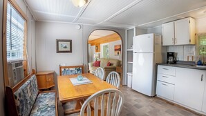 Ett kompakt kök med vita skåp, ett matbord i trä och en soffa med mönstrade kuddar.