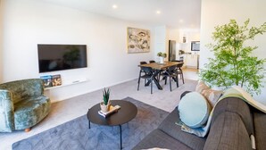 Ein modernes Wohnzimmer mit Flachbildfernseher, einer Couch, einem Couchtisch und einem Essbereich mit Stühlen.