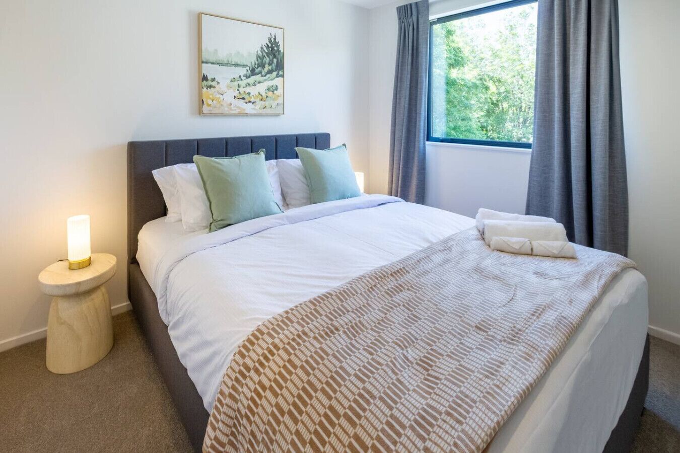 A neatly made bed with a patterned throw, a bedside lamp, and a painting above it.