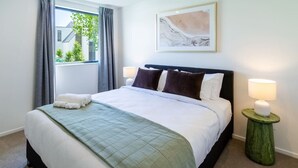 Ein ordentlich bezogenes Bett mit einer grünen Decke, zwei Nachttischlampen und einem gerahmten abstrakten Gemälde an der Wand.
