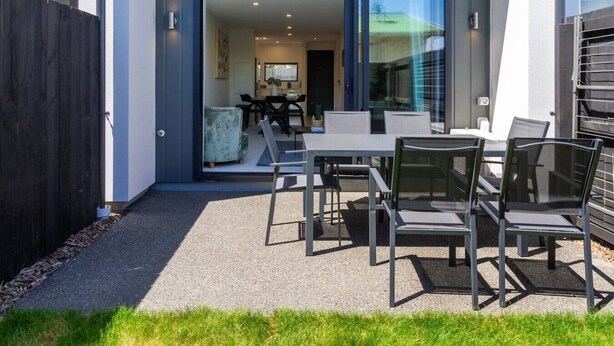 Eine moderne Außenpatio mit Tisch und Stühlen, eine Schiebetür zu einem Innenbereich mit Essbereich und ein dunkler Zaun, der den Bereich umgibt.