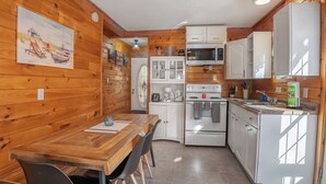 Un intérieur en bois comprenant une table à manger, des chaises, une cuisine avec des meubles blancs, un four à micro-ondes et une cuisinière.