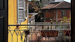 Een balkon met een gele muur, een metalen hekwerk en plantenbakken.