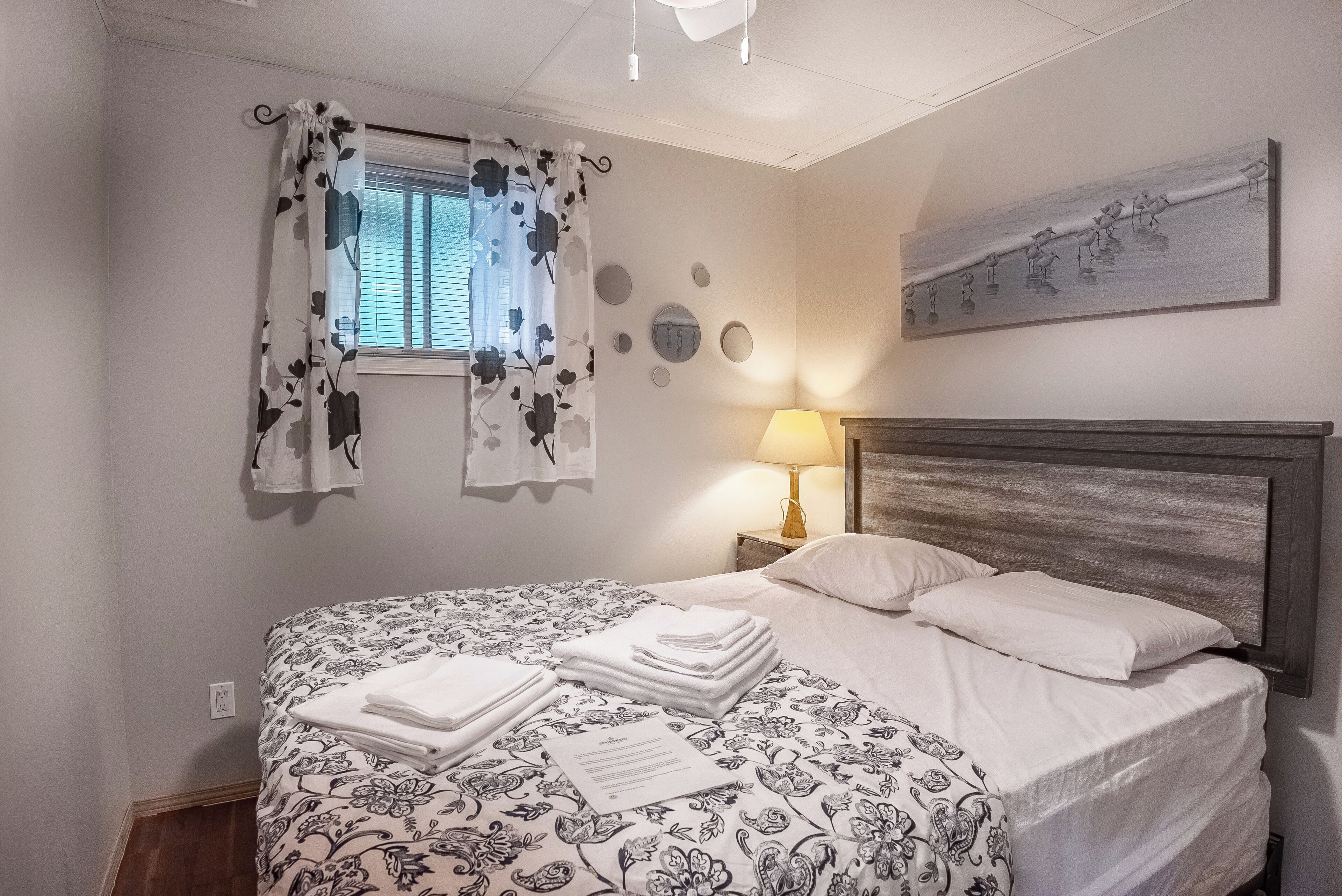 Uma cama bem arrumada com colcha estampada, um abajur e uma obra de arte na parede.