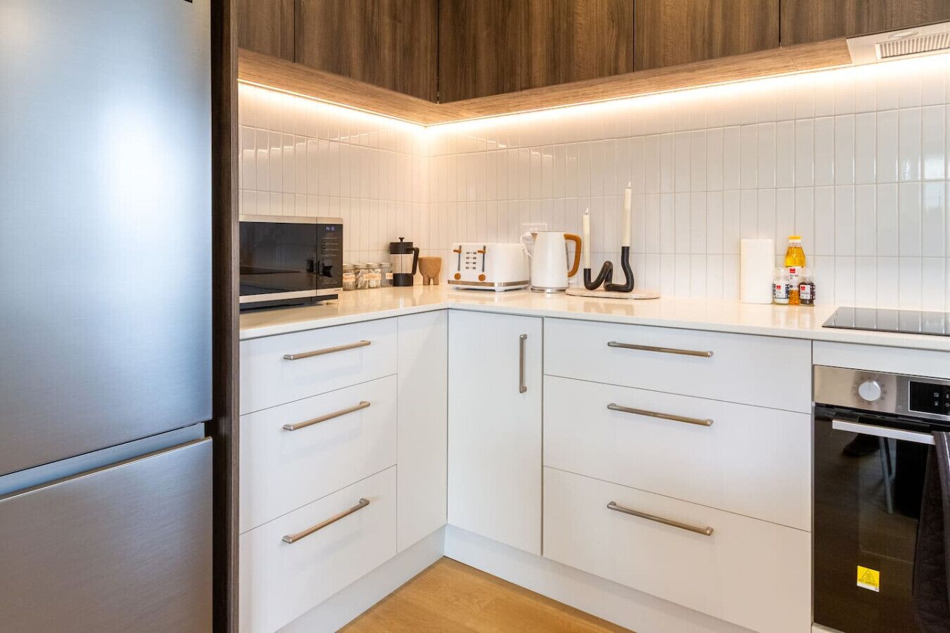 A modern kitchen with white cabinets, stainless steel appliances, and a wooden ceiling.