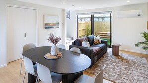 Un salon moderne avec une table à manger, des chaises grises, un canapé avec des coussins et un tapis à motifs.